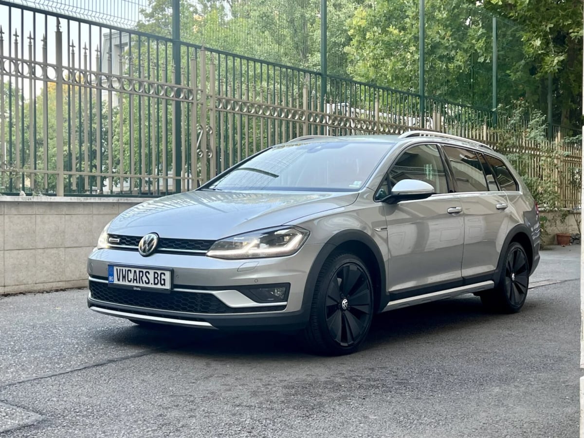 Сребристо комби Volkswagen Golf Alltrack, паркирано до ограда, с табела на автокъща вместо номер
